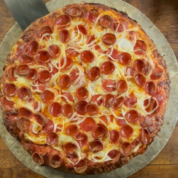 Cosmic Pizza's pepperoni and onion pizza, fresh from the oven, on a round pizza tray.
