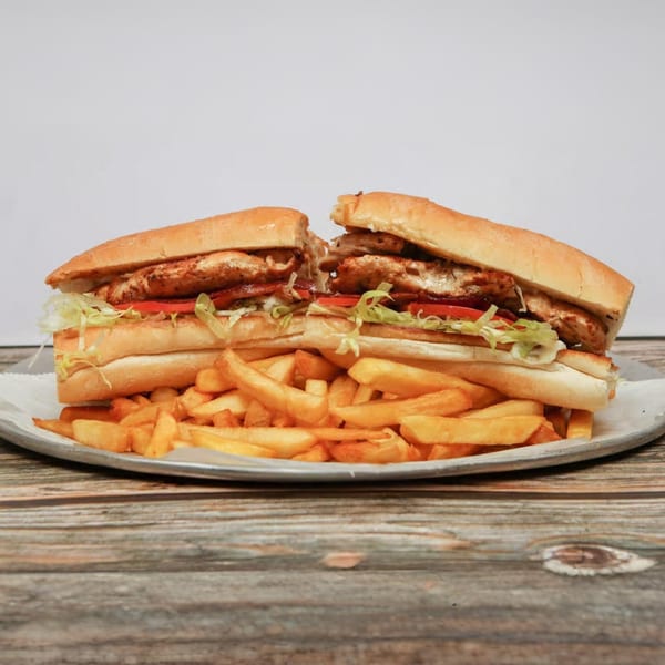 A large grilled chicken sub sandwich, cut in half, served with a generous portion of french fries.