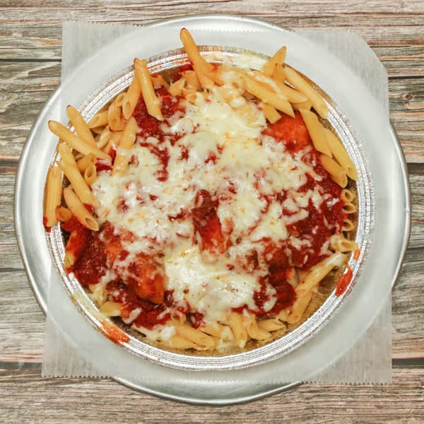 Baked penne pasta with red sauce and melted cheese in a foil pan on a wooden table.